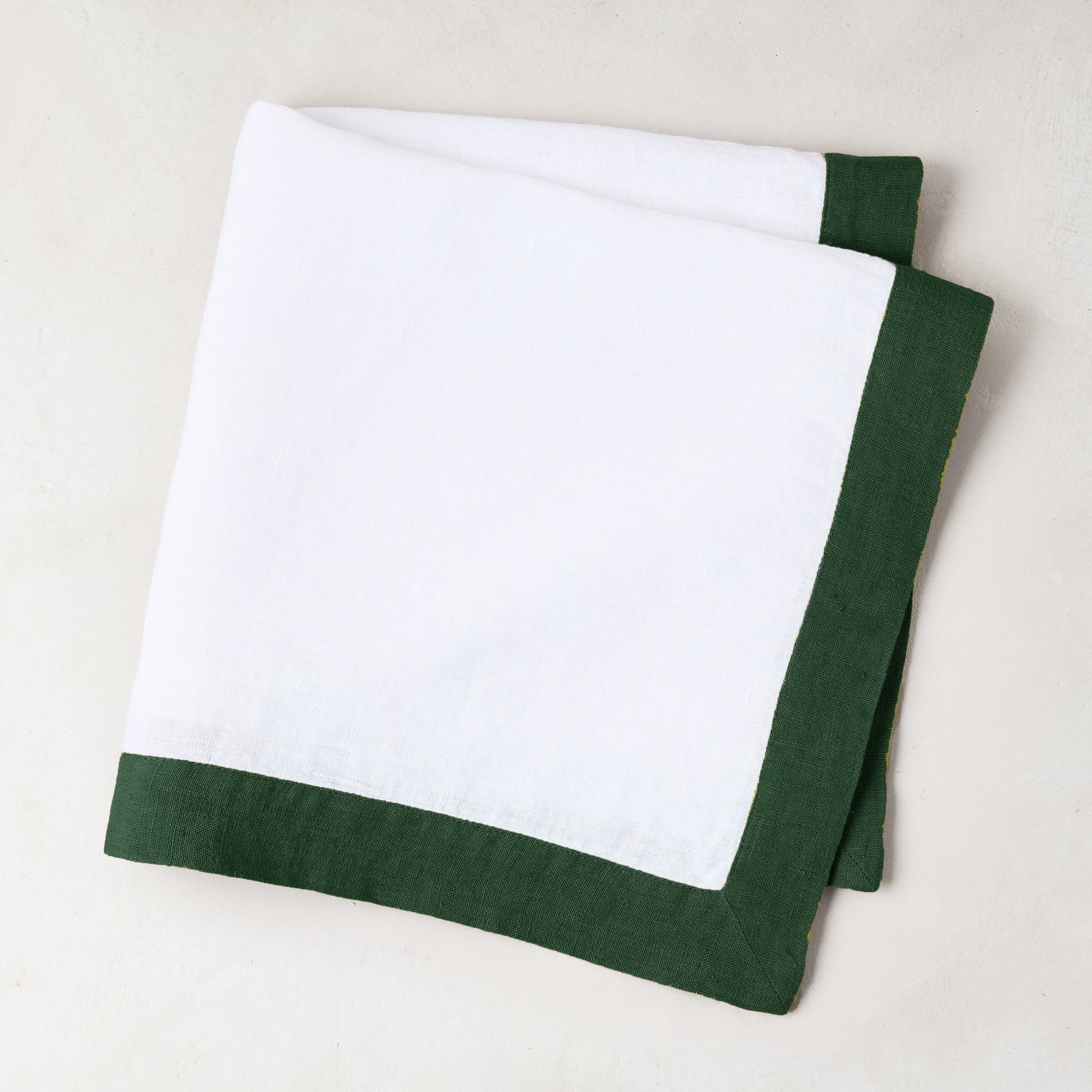 Folded white linen napkin with a fir green border.