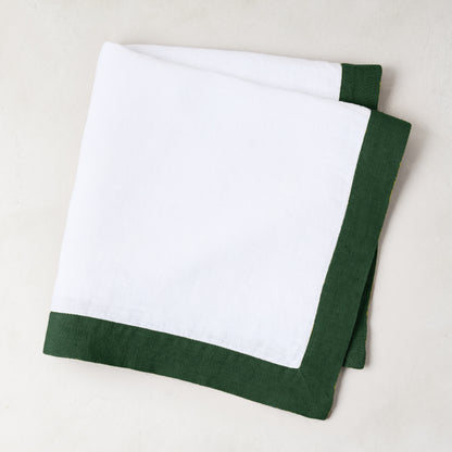 Folded white linen napkin with a fir green border.
