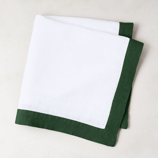 Folded white linen napkin with a fir green border.