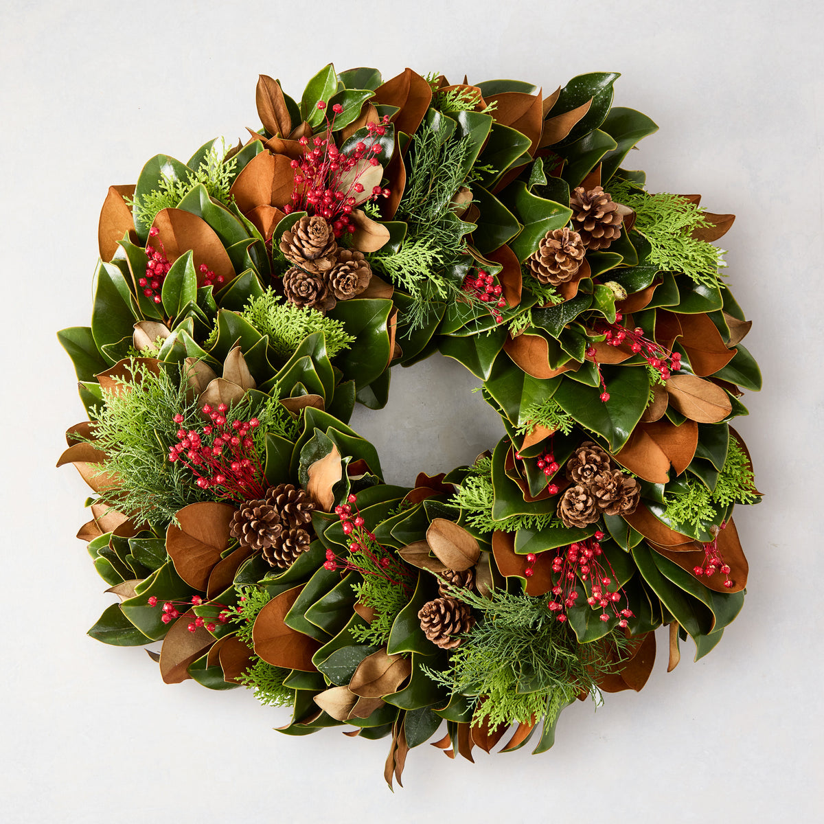 24-inch holiday wreath featuring fresh magnolia leaves, red berries, Carolina Sapphire greenery, and miniature pinecones.
