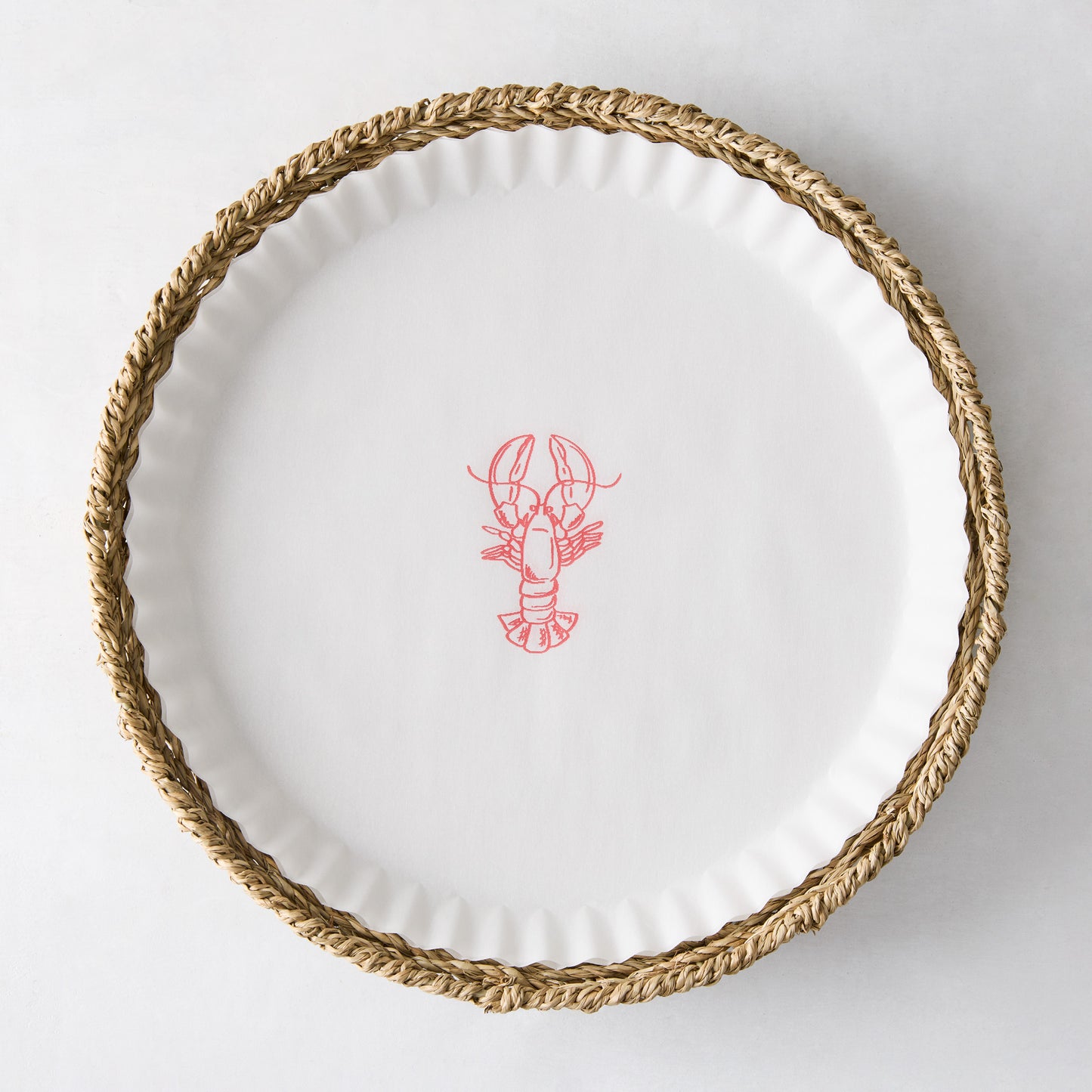 Round white parchment liner with a red lobster illustration, set inside a woven straw basket.
