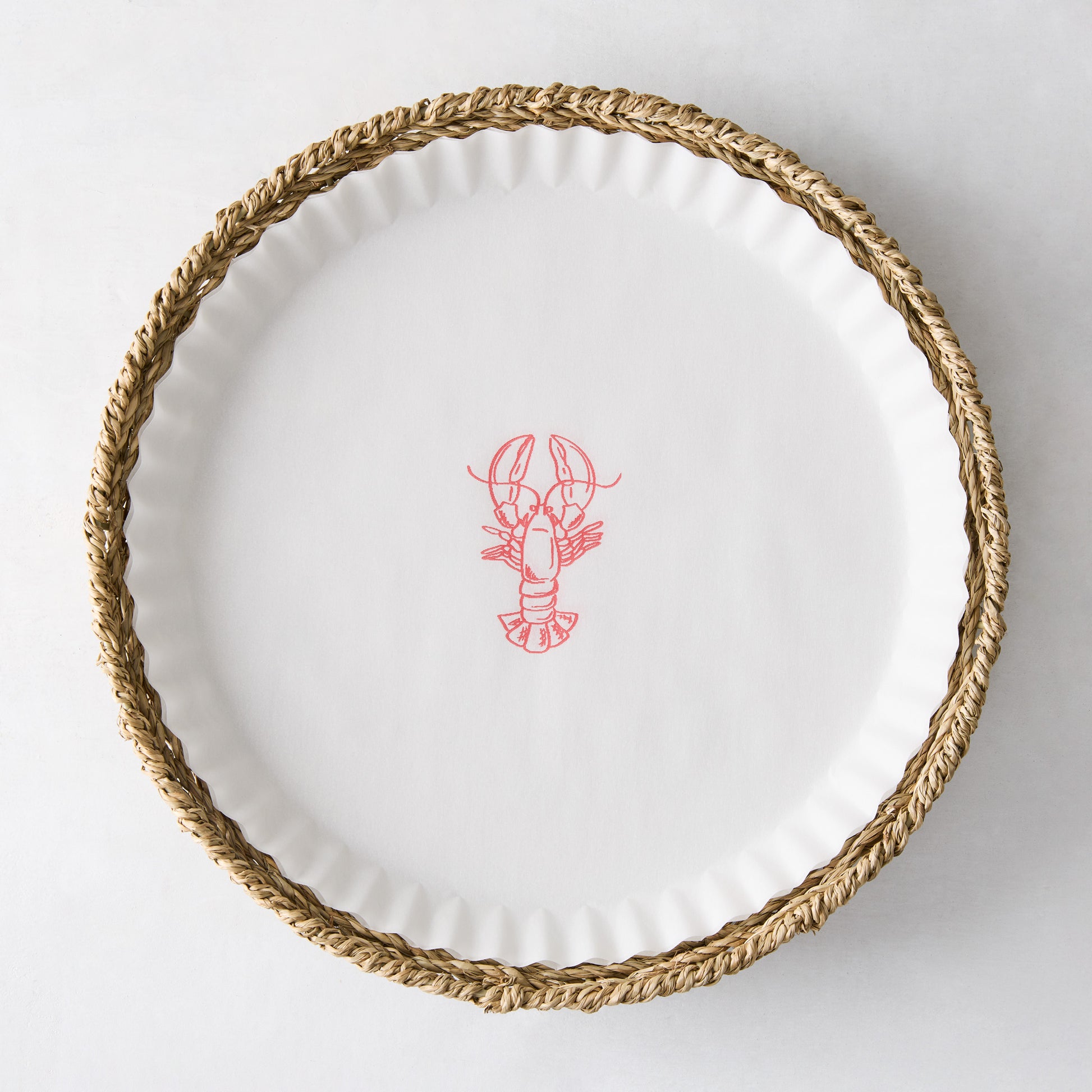 Round white parchment liner with a red lobster illustration, set inside a woven straw basket.