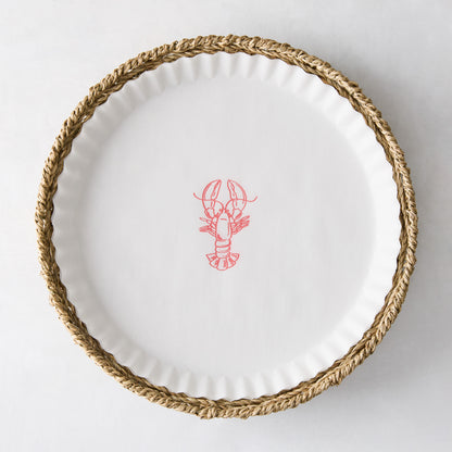 Round white parchment liner with a red lobster illustration, set inside a woven straw basket.
