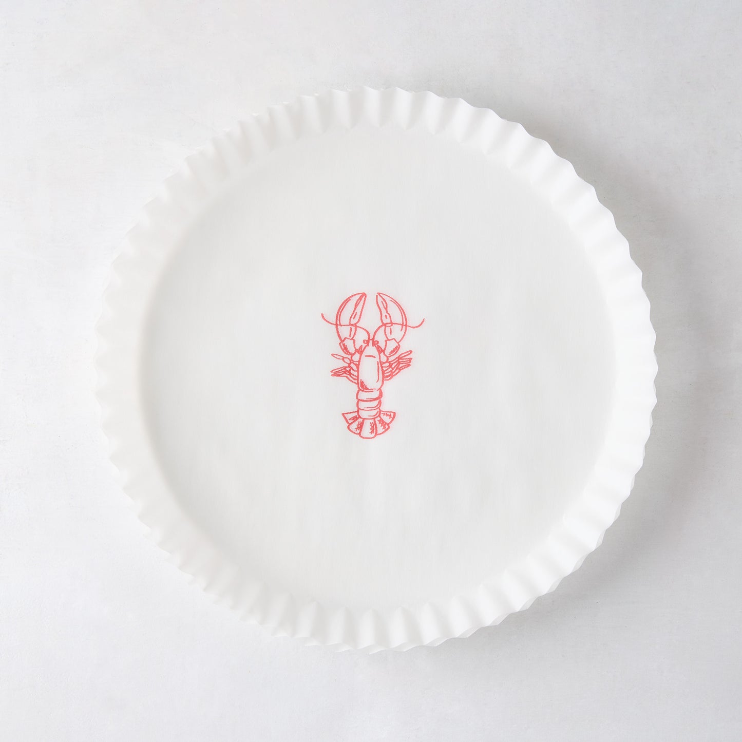 White round parchment liner with ruffled edges and a red lobster illustration in the center.