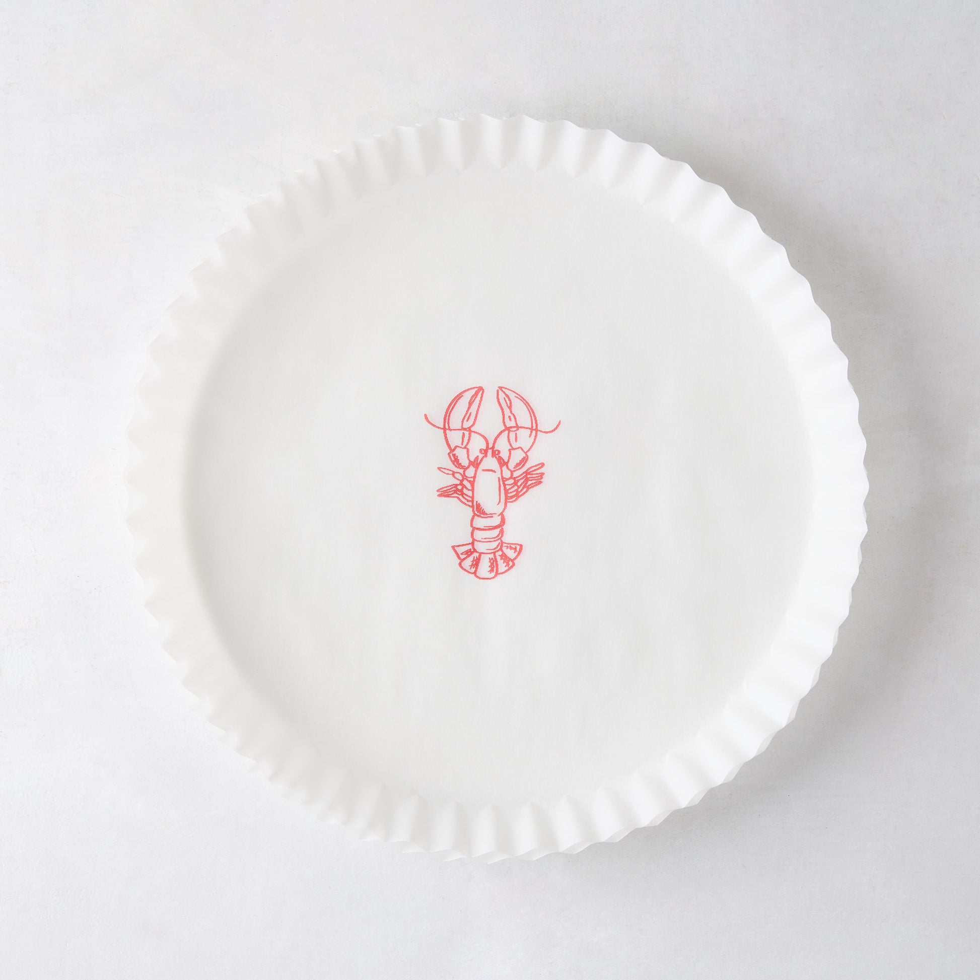 White round parchment liner with ruffled edges and a red lobster illustration in the center.