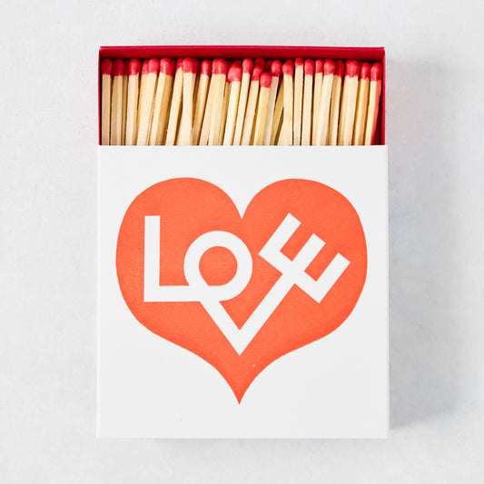 Oversized white matchbox with a red heart and "LOVE" text, filled with long wooden matches with red tips.
