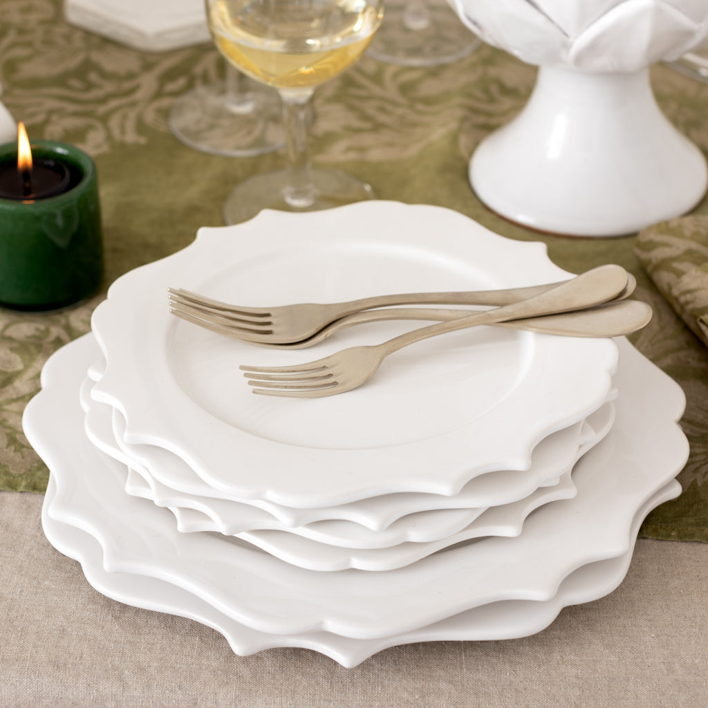 Stack of white ceramic Lungarno dinner plates with sculptural edges, 11" diameter, on a table setting.