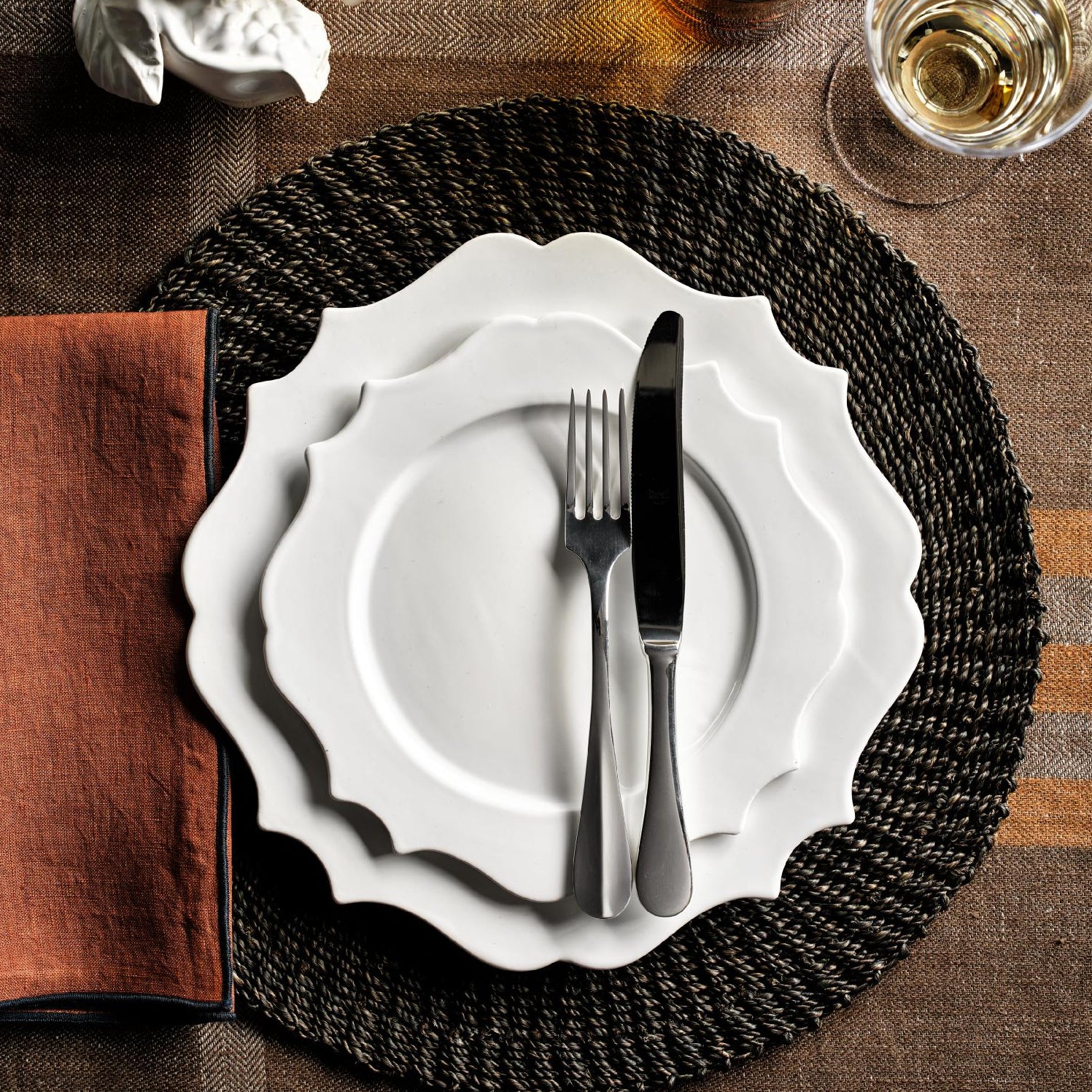 9-inch white ceramic Lungarno salad plate with sculptural scalloped edges, set on a woven placemat with cutlery.