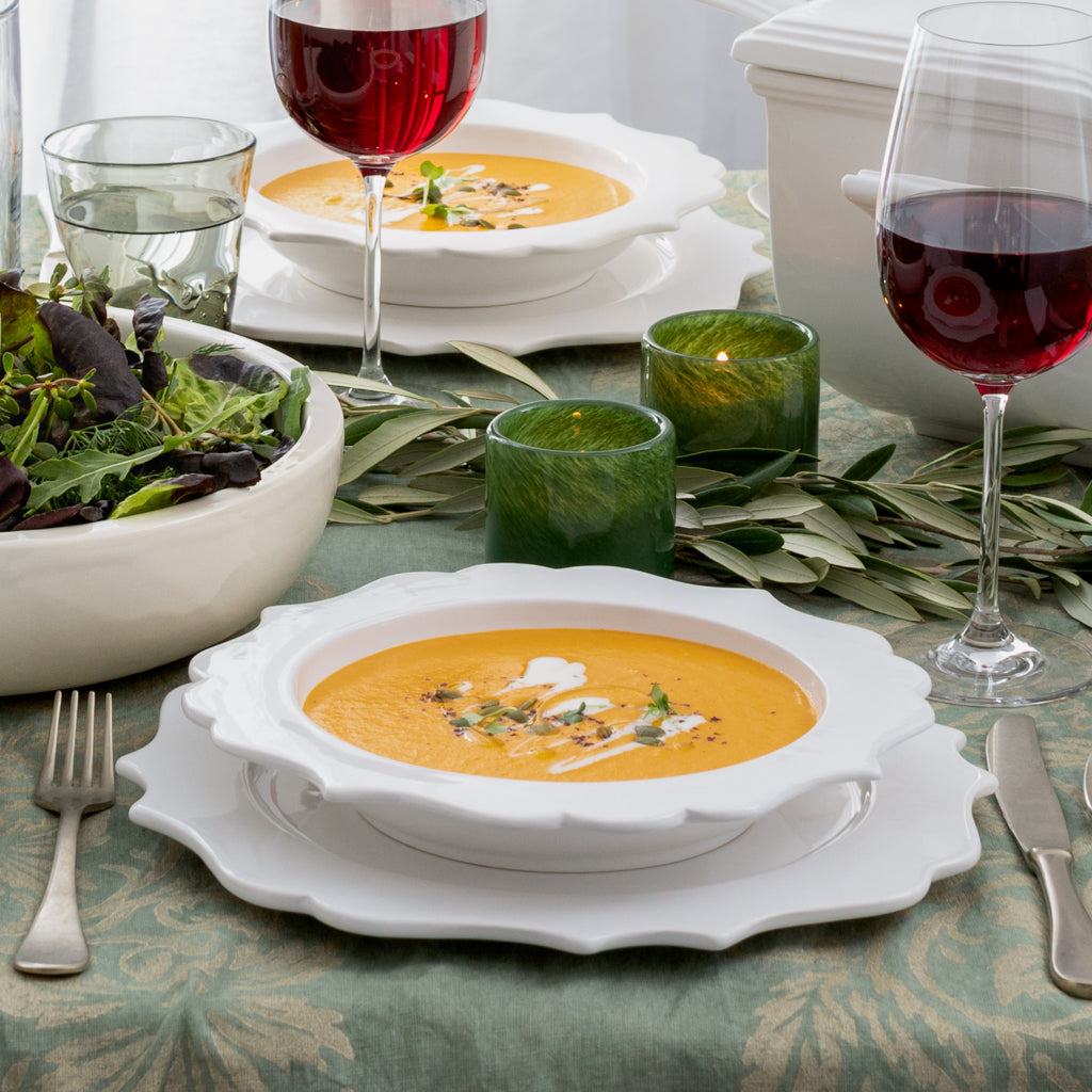 White ceramic Lungarno soup bowl with sculptural detail, filled with orange soup, on a green tablecloth.