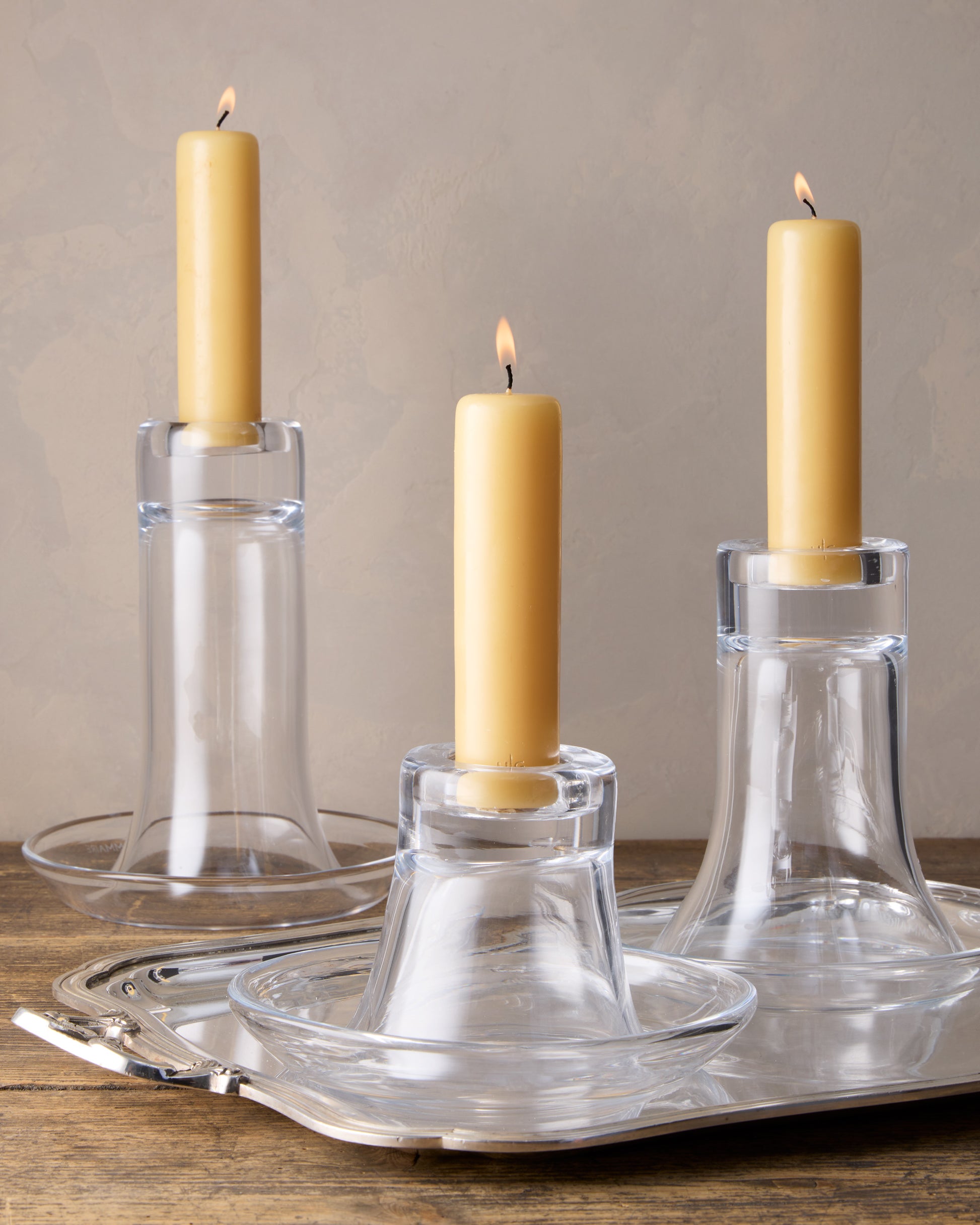 Three clear glass Luz Medium Candleholders with amber pillar candles on a silver tray.