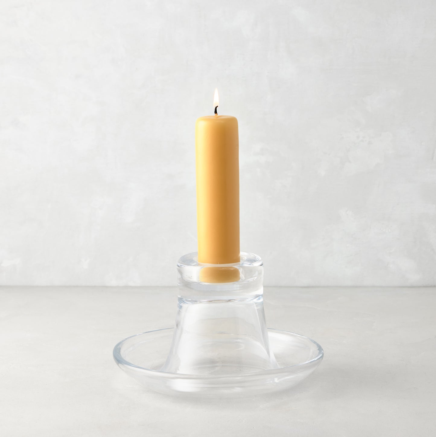 Small clear glass Luz Candleholder with a lit amber pillar candle.