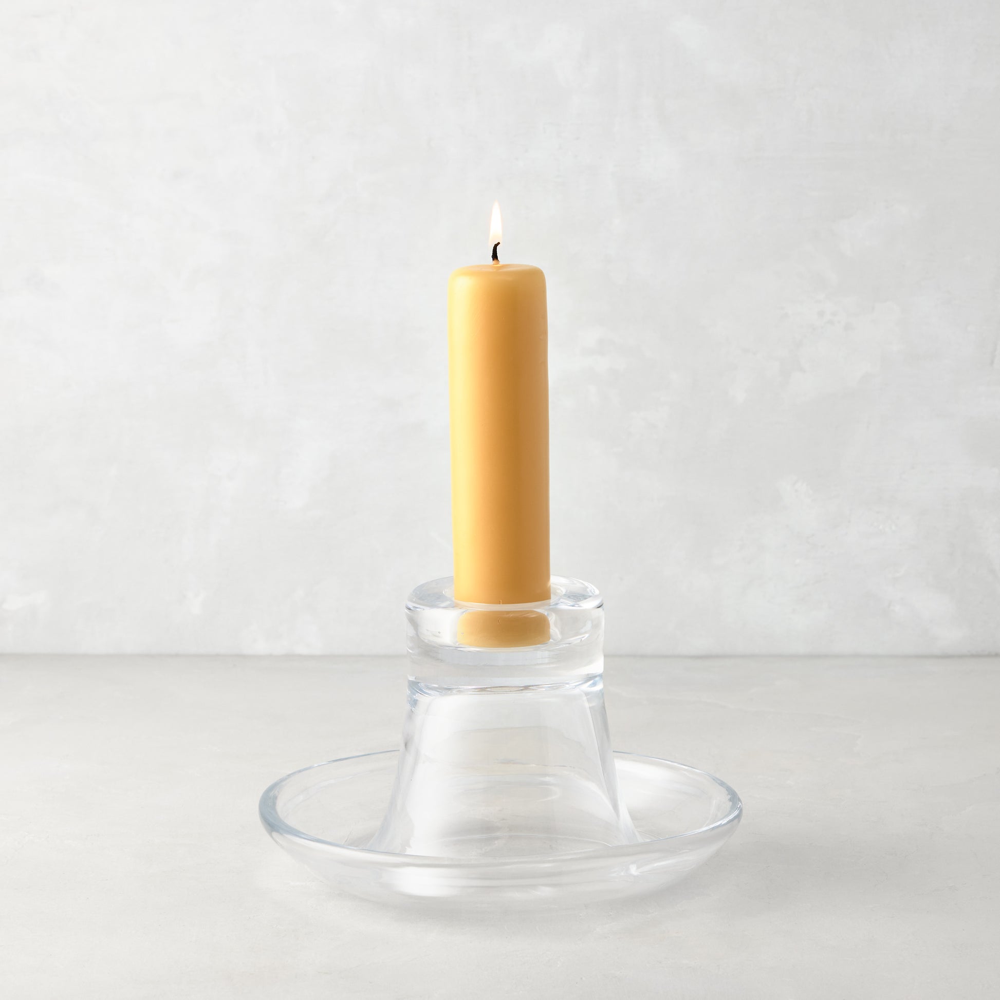 Small clear glass Luz Candleholder with a lit amber pillar candle.