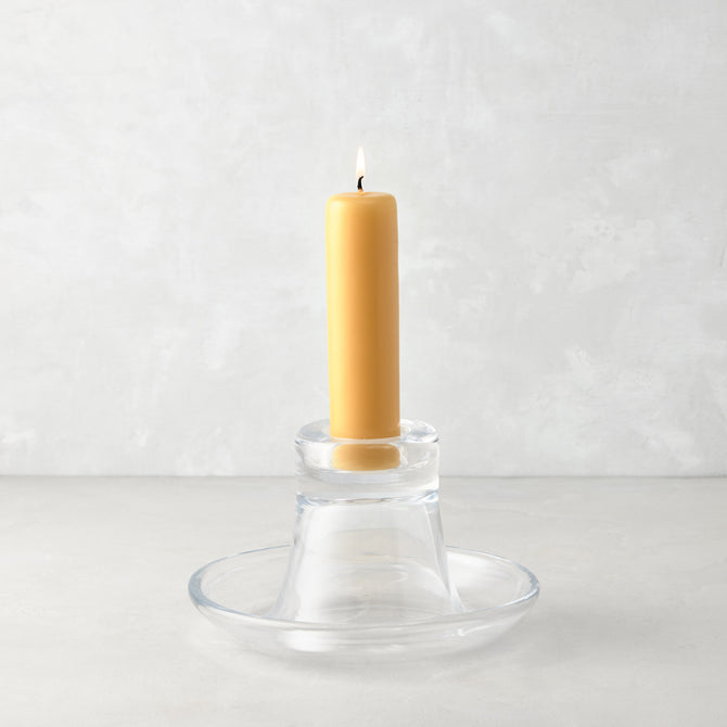 Small clear glass Luz Candleholder with a lit amber pillar candle.