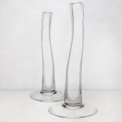Two clear, tall, slender glass vases with scissor-cut mouths and wide bases.