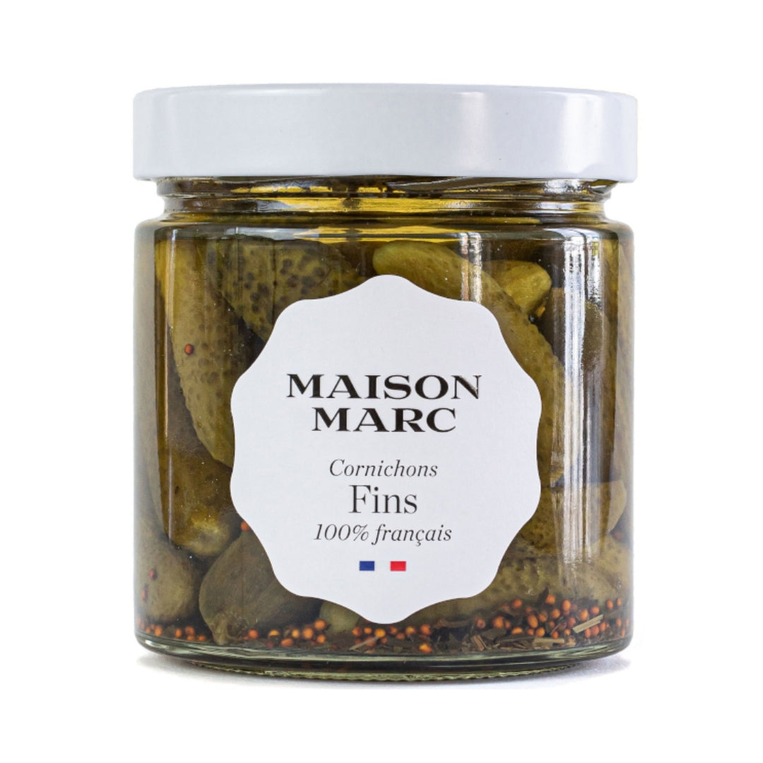 Maison Marc Cornichons Fins in a clear glass jar with a white lid and label, showing whole green pickles and spices.