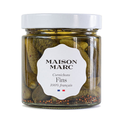 Maison Marc Cornichons Fins in a clear glass jar with a white lid and label, showing whole green pickles and spices.