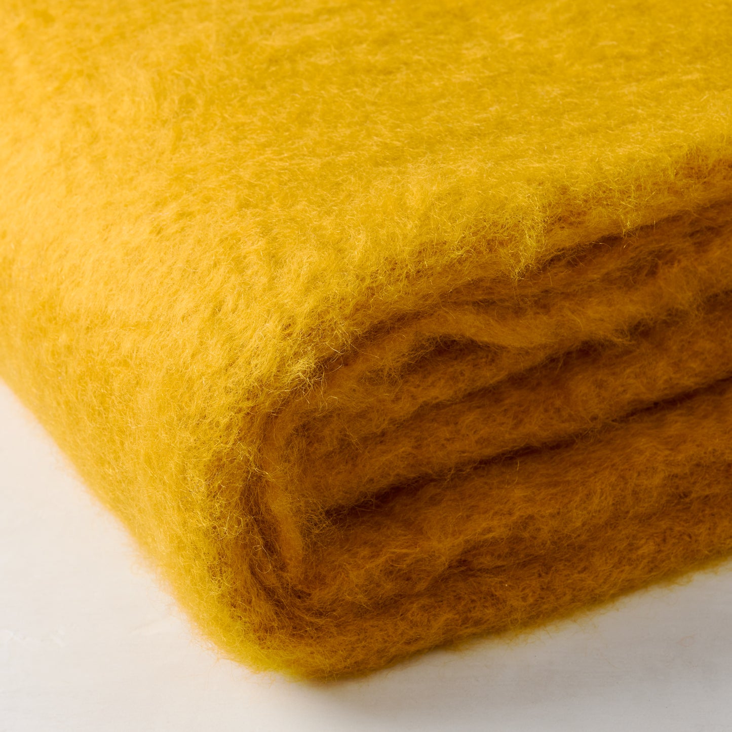 Folded Mantas Ezcaray yellow mustard mohair throw, handwoven with soft, vibrant fibers.