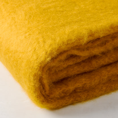 Folded Mantas Ezcaray yellow mustard mohair throw, handwoven with soft, vibrant fibers.