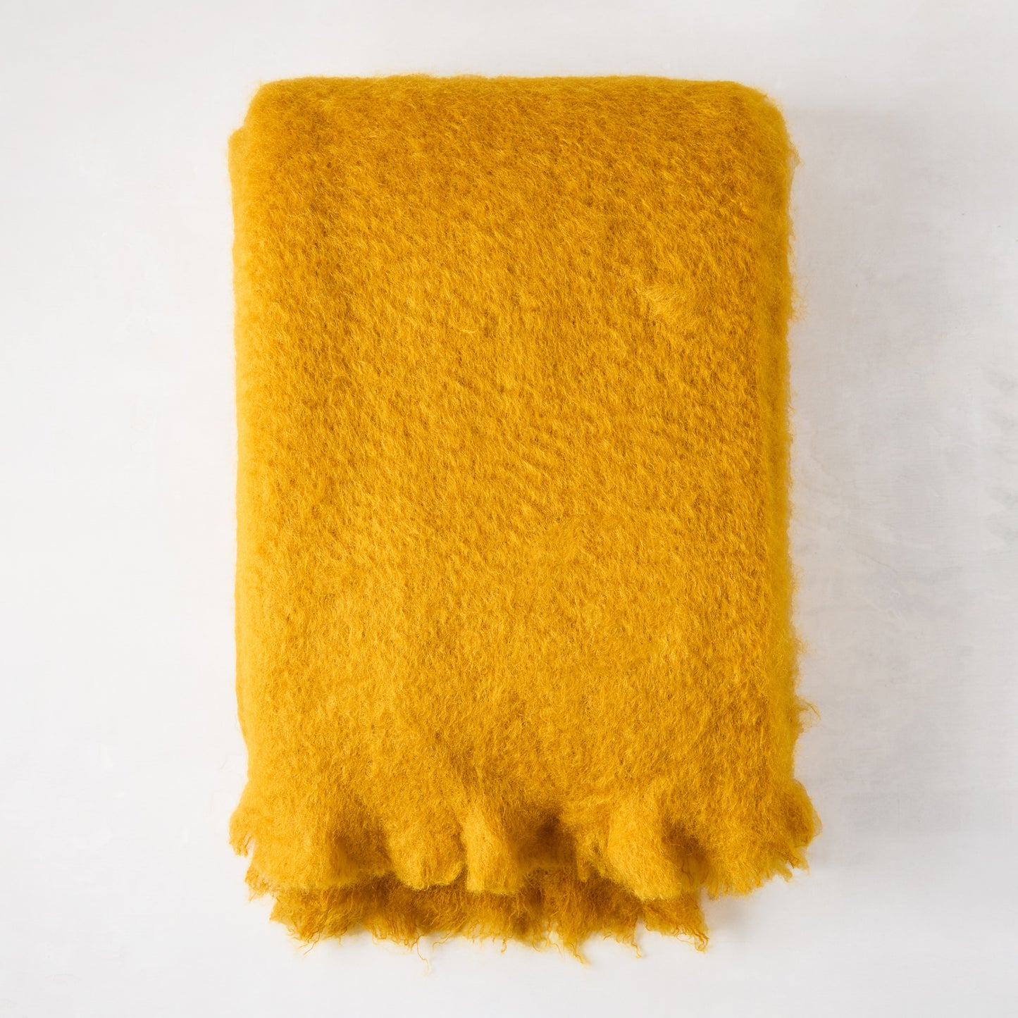 Vibrant yellow mustard mohair throw, folded, with a soft, shaggy texture and fringed edge.