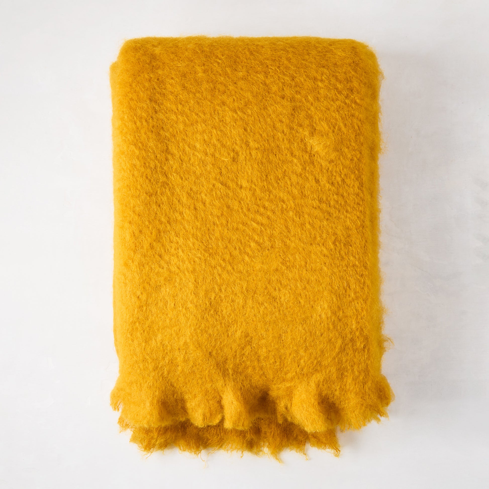 Vibrant yellow mustard mohair throw, folded, with a soft, shaggy texture and fringed edge.