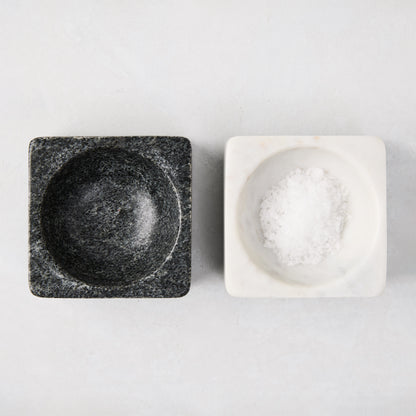 Black and white square marble pinch bowls, one filled with white salt, on a light background.