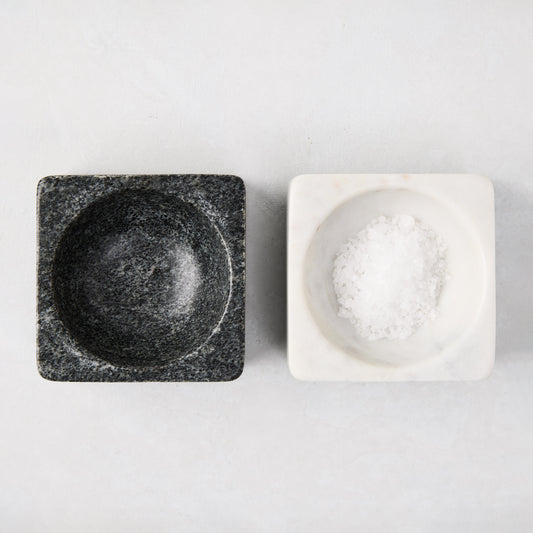 Black and white square marble pinch bowls, one filled with white salt, on a light background.
