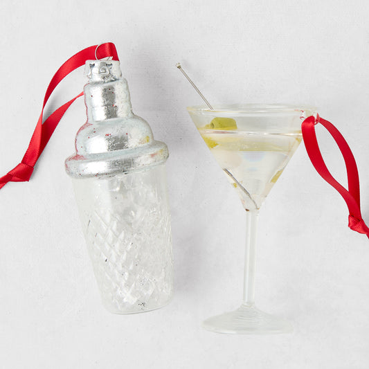 Glass cocktail shaker and martini ornament set with red hanging ribbons on a white background.