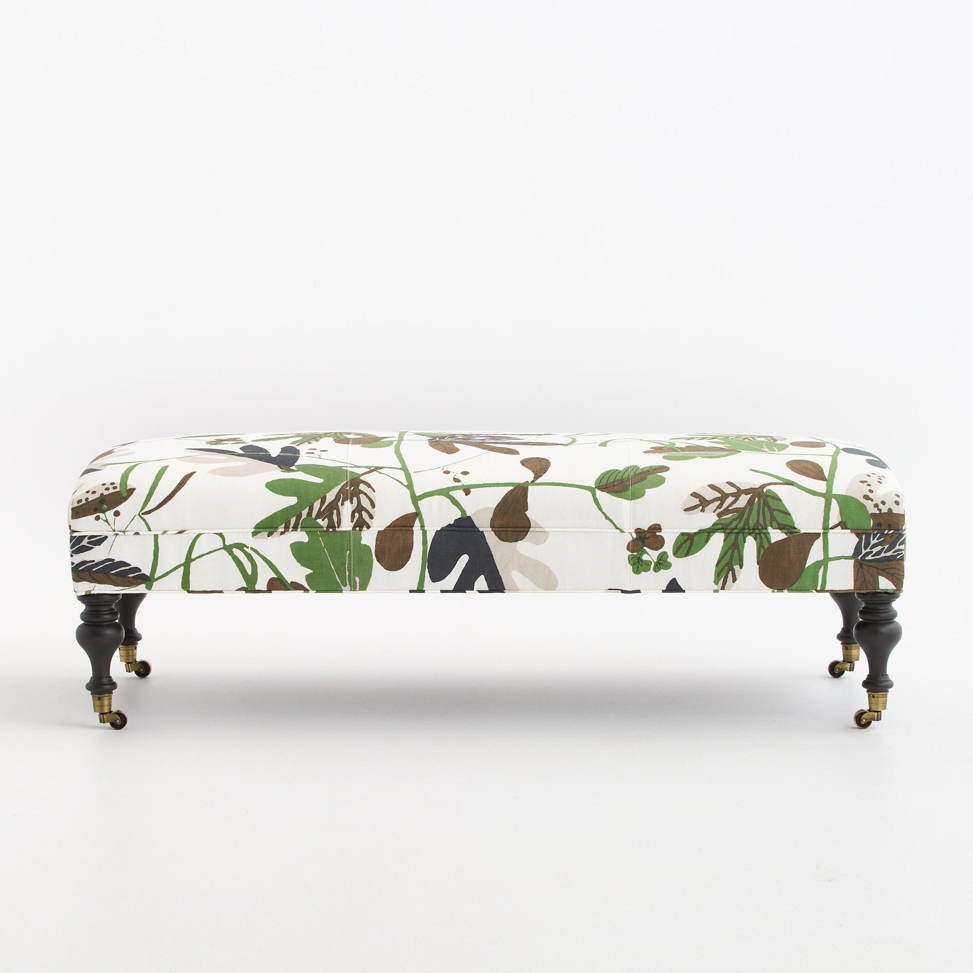 Matisse leaf botanical ottoman with ivory fabric, green foliage print, and black walnut legs on brass casters.