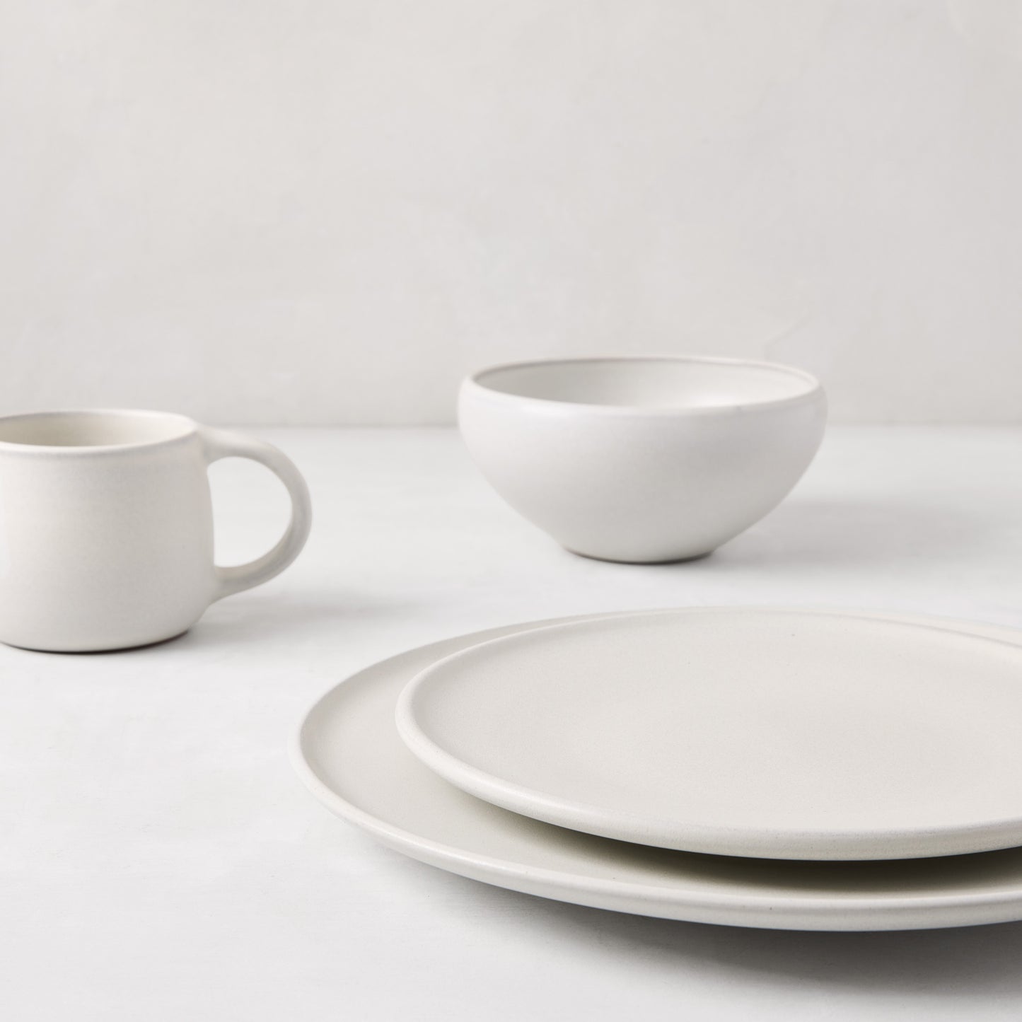 Matte white stoneware dinner plate, bowl, and mug with subtle grey speckles.