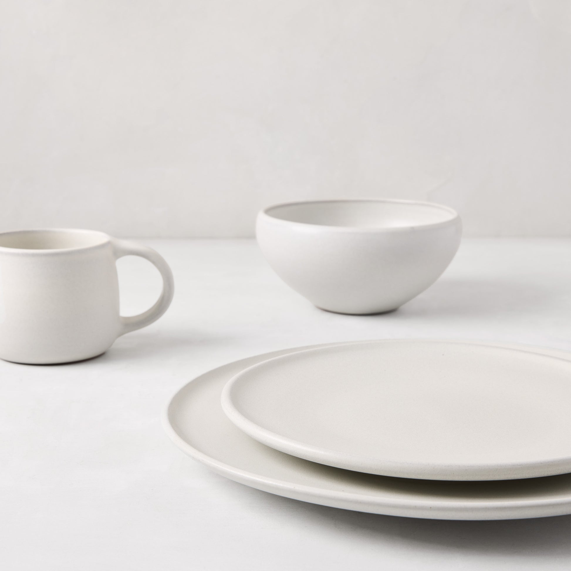 Matte white stoneware dinner plate, bowl, and mug with subtle grey speckles.