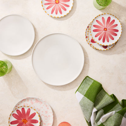 Matte white stoneware dinner plate, round and smooth, surrounded by colorful floral plates and green glasses.