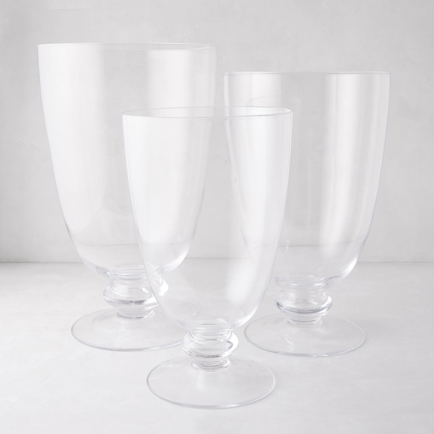 Three clear glass Mayfair hurricanes with decorative bases, varying in height.