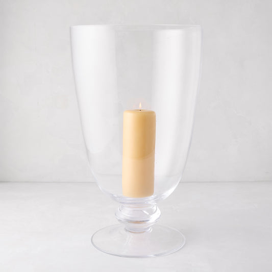 Large Mayfair clear glass hurricane with decorative base, holding a lit cream pillar candle.