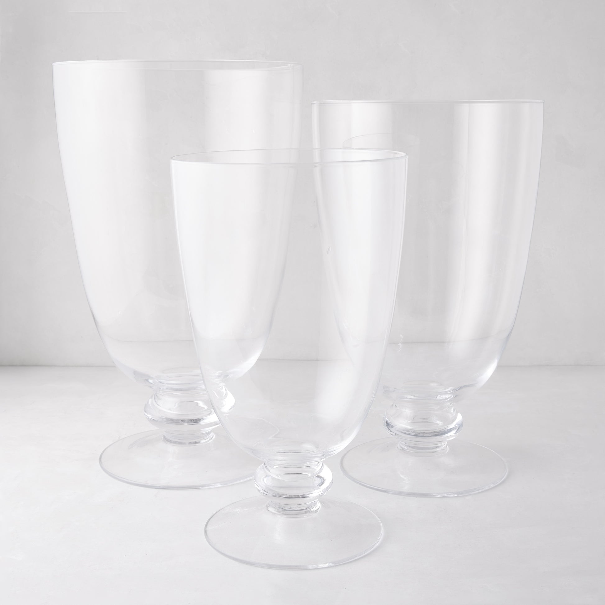 Three clear Mayfair Medium Glass Hurricanes with decorative bases, varying in height.