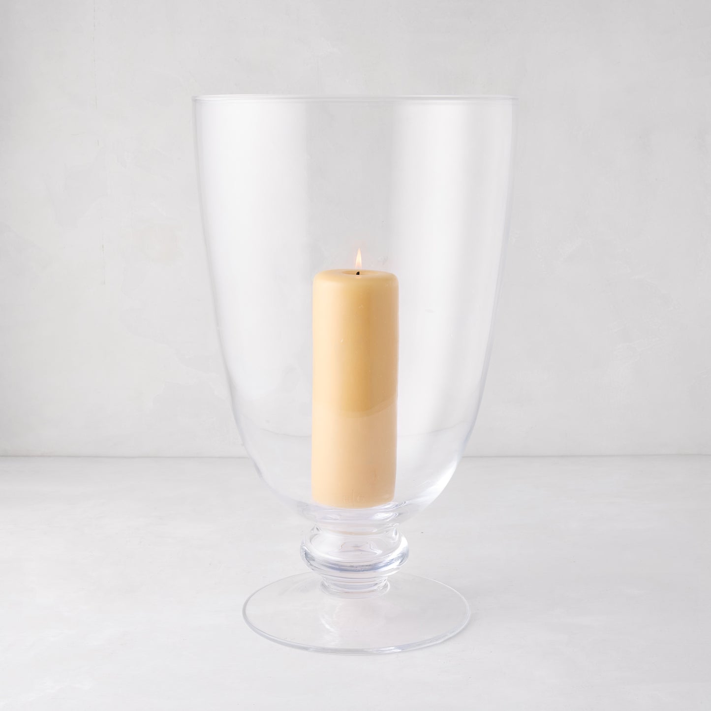 Mayfair Medium Glass Hurricane, clear glass with decorative base, holding a lit cream pillar candle.