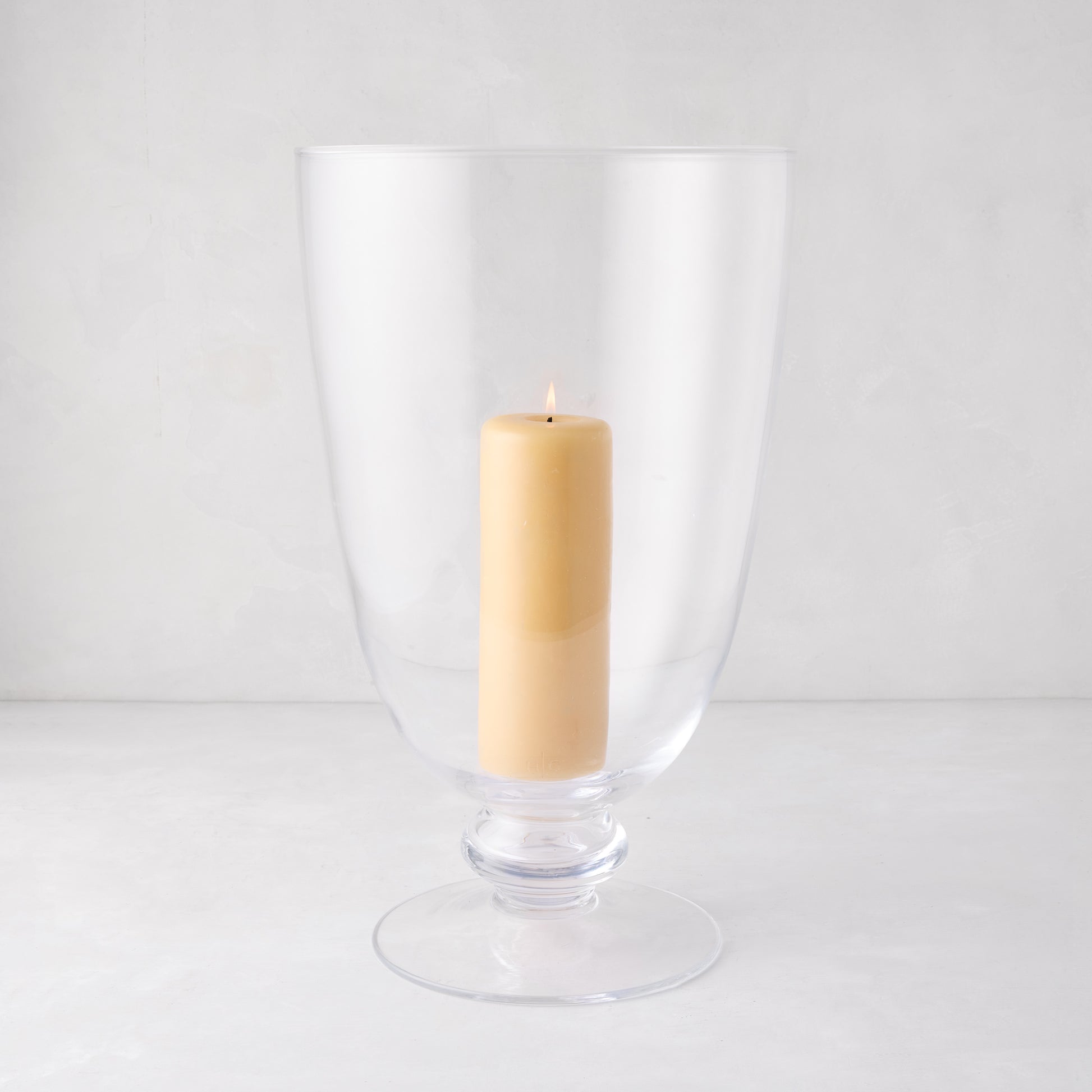 Mayfair Medium Glass Hurricane, clear glass with decorative base, holding a lit cream pillar candle.