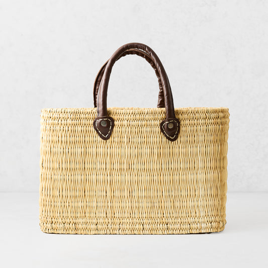 Medium rectangular woven palm grass tote bag with dark brown leather handles.