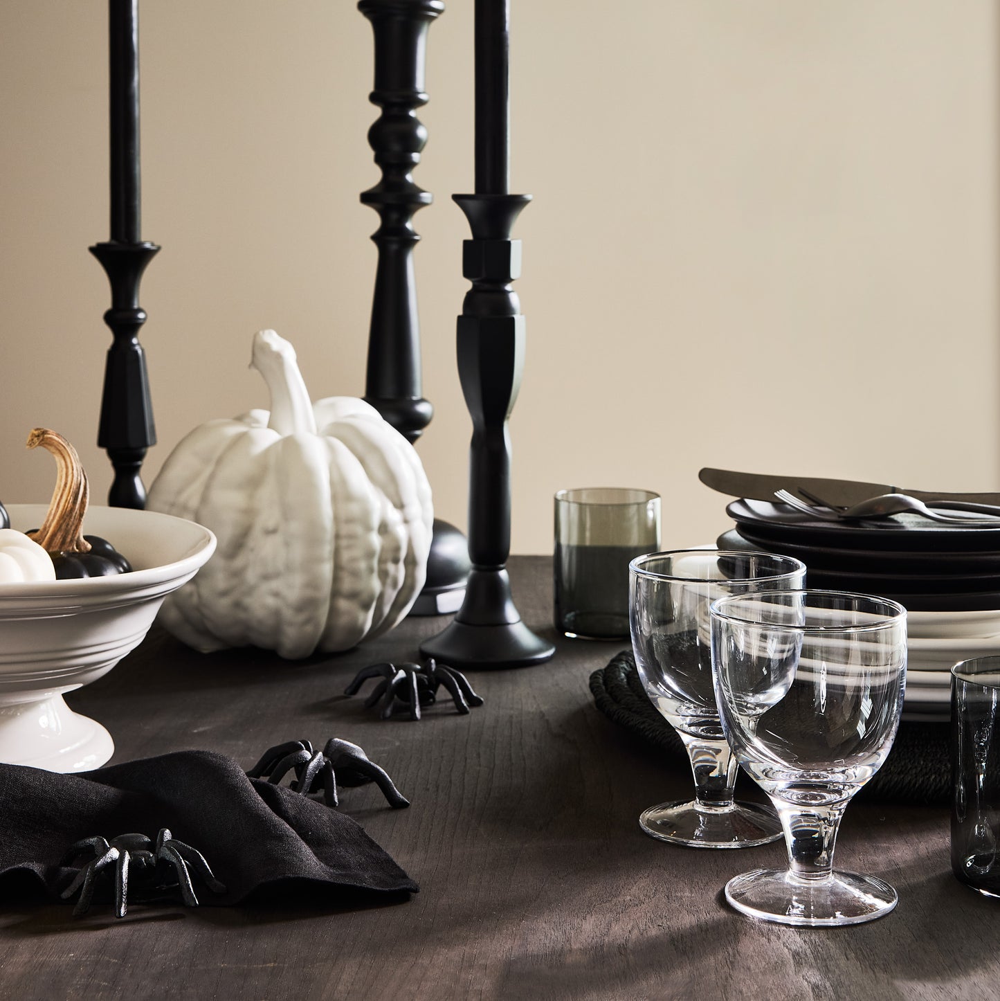 Small matte white ceramic pumpkin on a dark wooden table with black candlesticks, plates, and spider decor.