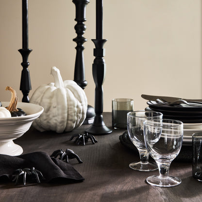 Small matte white ceramic pumpkin on a dark wooden table with black candlesticks, plates, and spider decor.