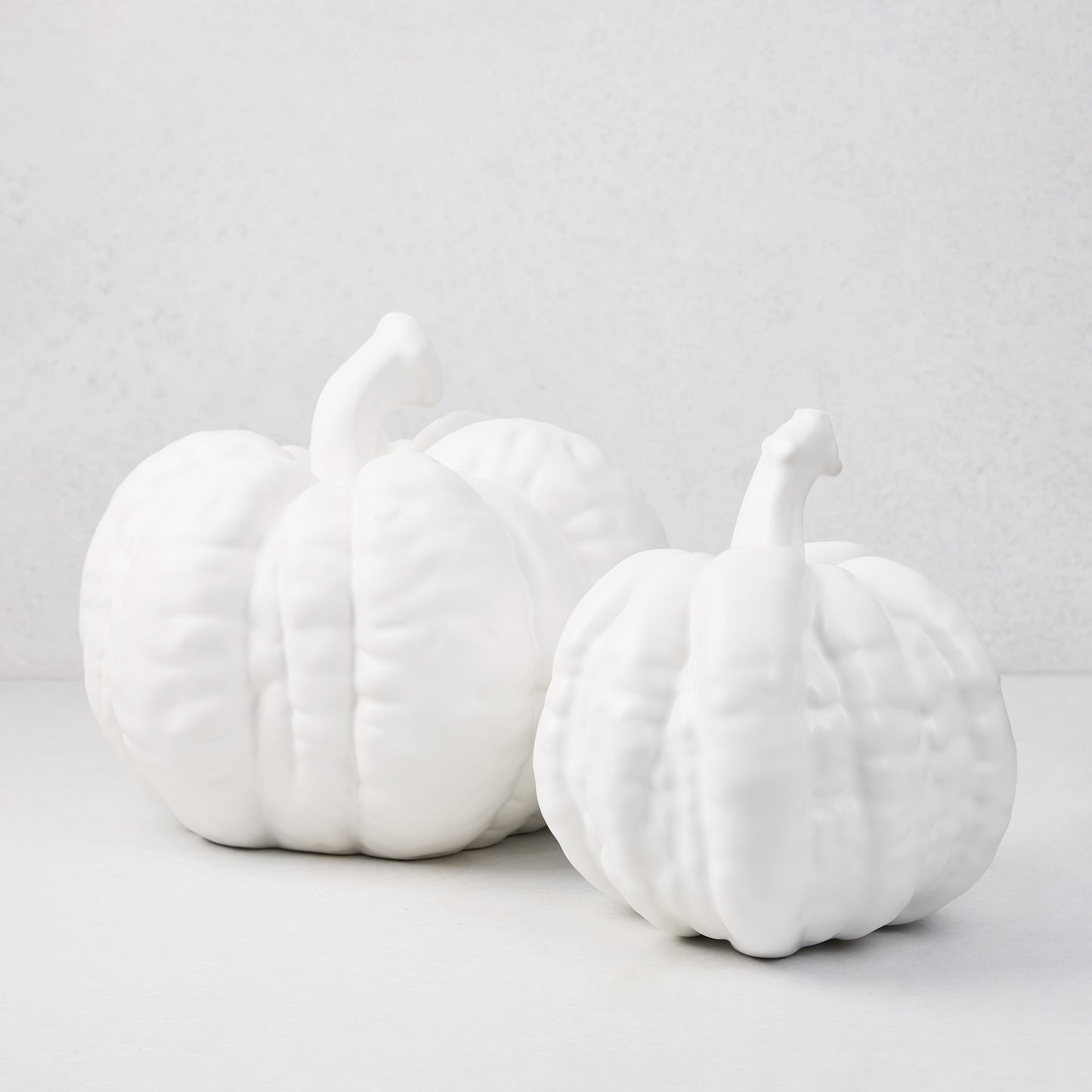 Two matte white ceramic pumpkins, one small and one large, with textured ridges and stems.