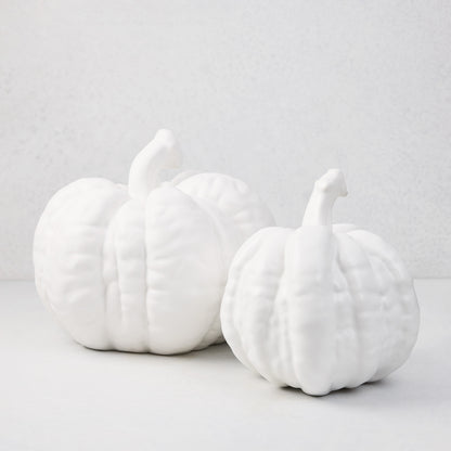 Two matte white ceramic pumpkins, one small and one large, with textured ridges and stems.