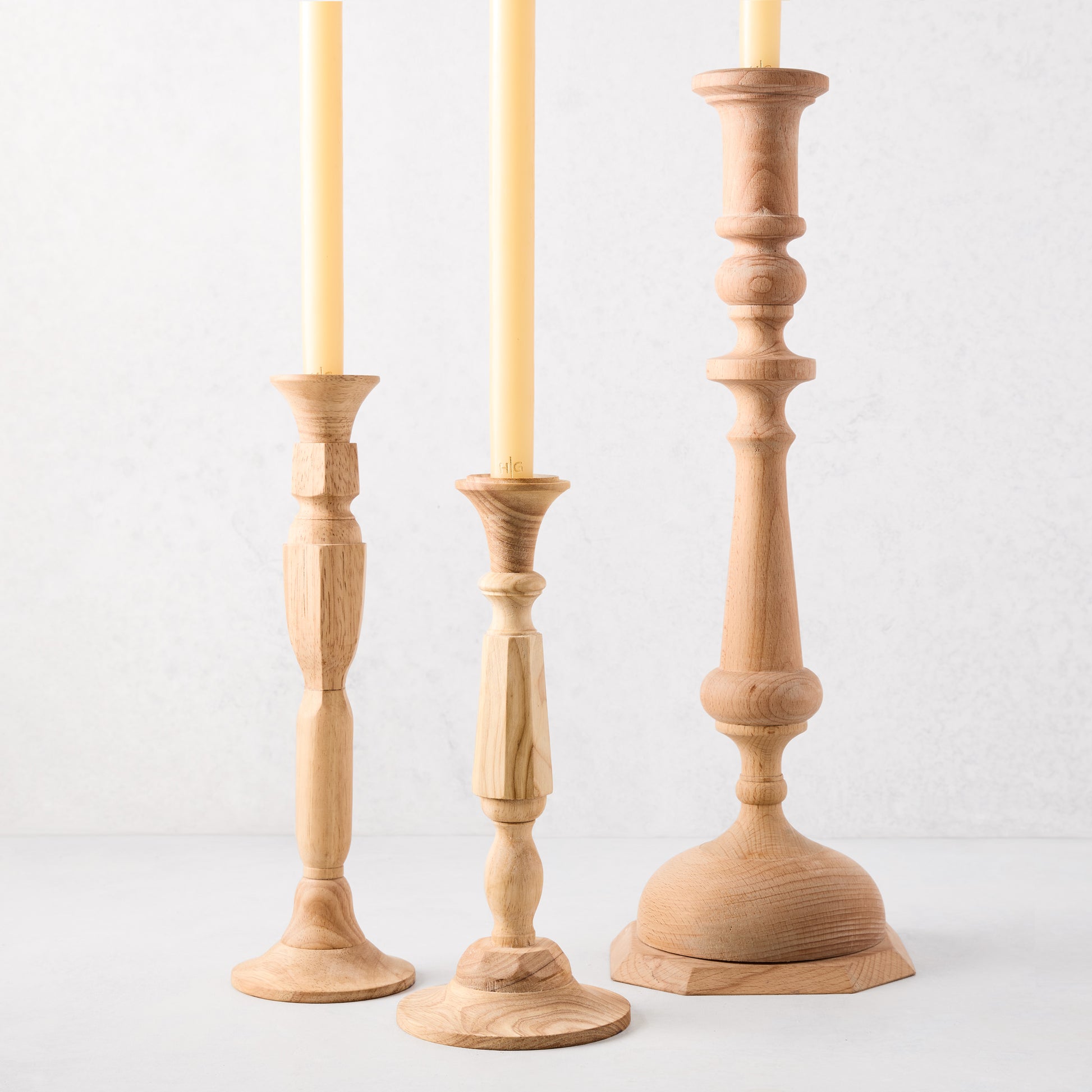 Three natural beechwood Georgian candlesticks, varying heights, with yellow taper candles.