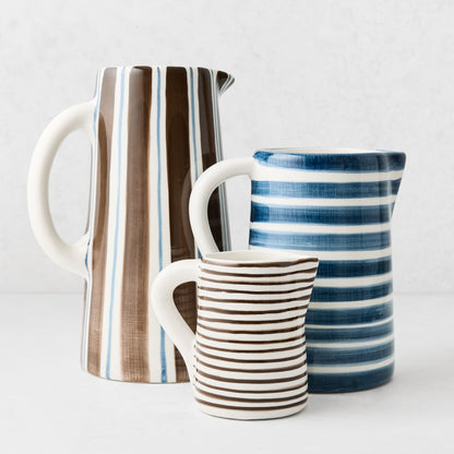 Three ceramic pitchers in varying sizes with hand-painted blue and brown striped patterns on a white background.