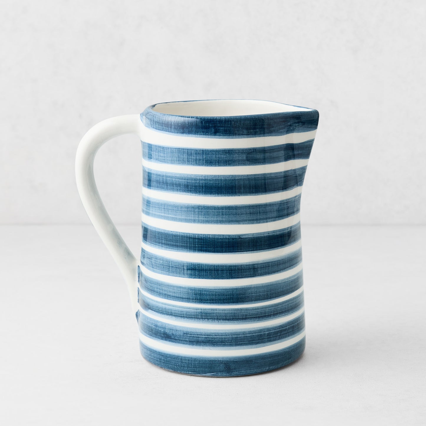 Medium Salerno ceramic pitcher with hand-painted navy blue and white horizontal stripes and a curved handle.