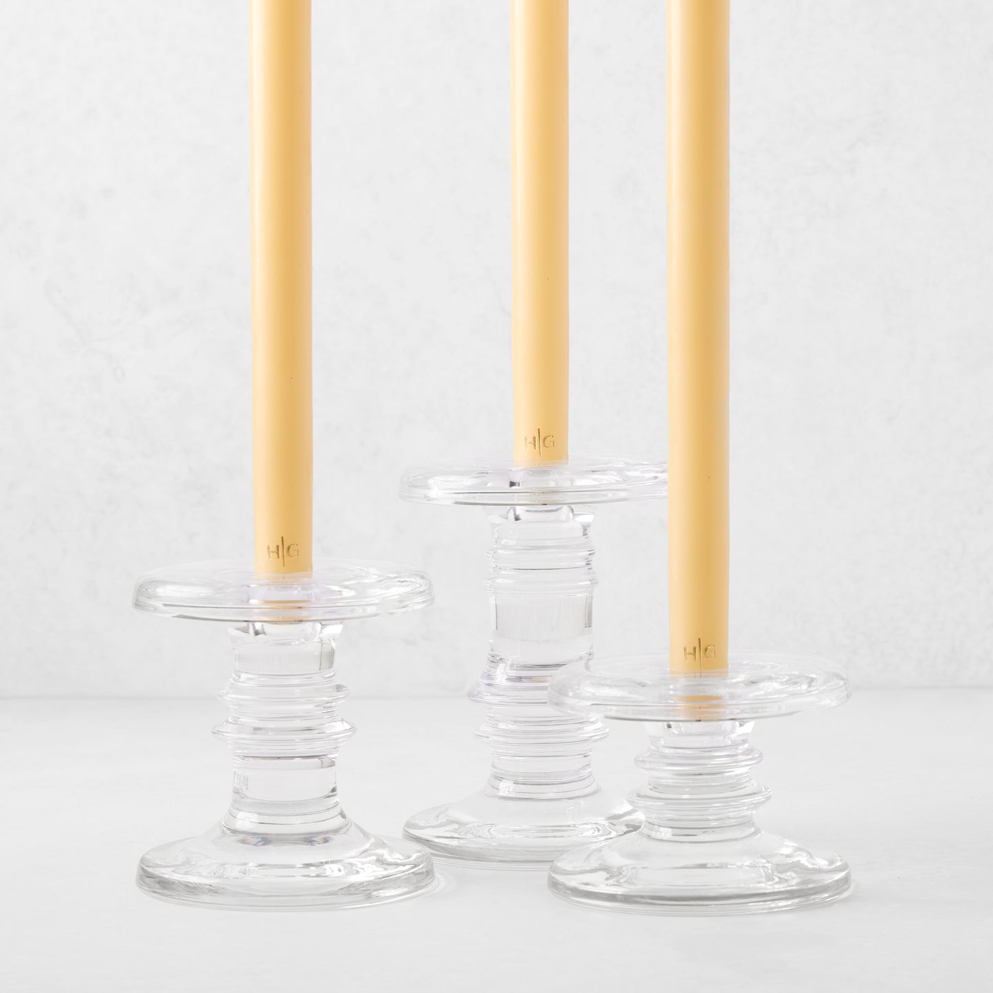 Three clear glass taper candleholders of varying heights with ridged bases, holding yellow taper candles.