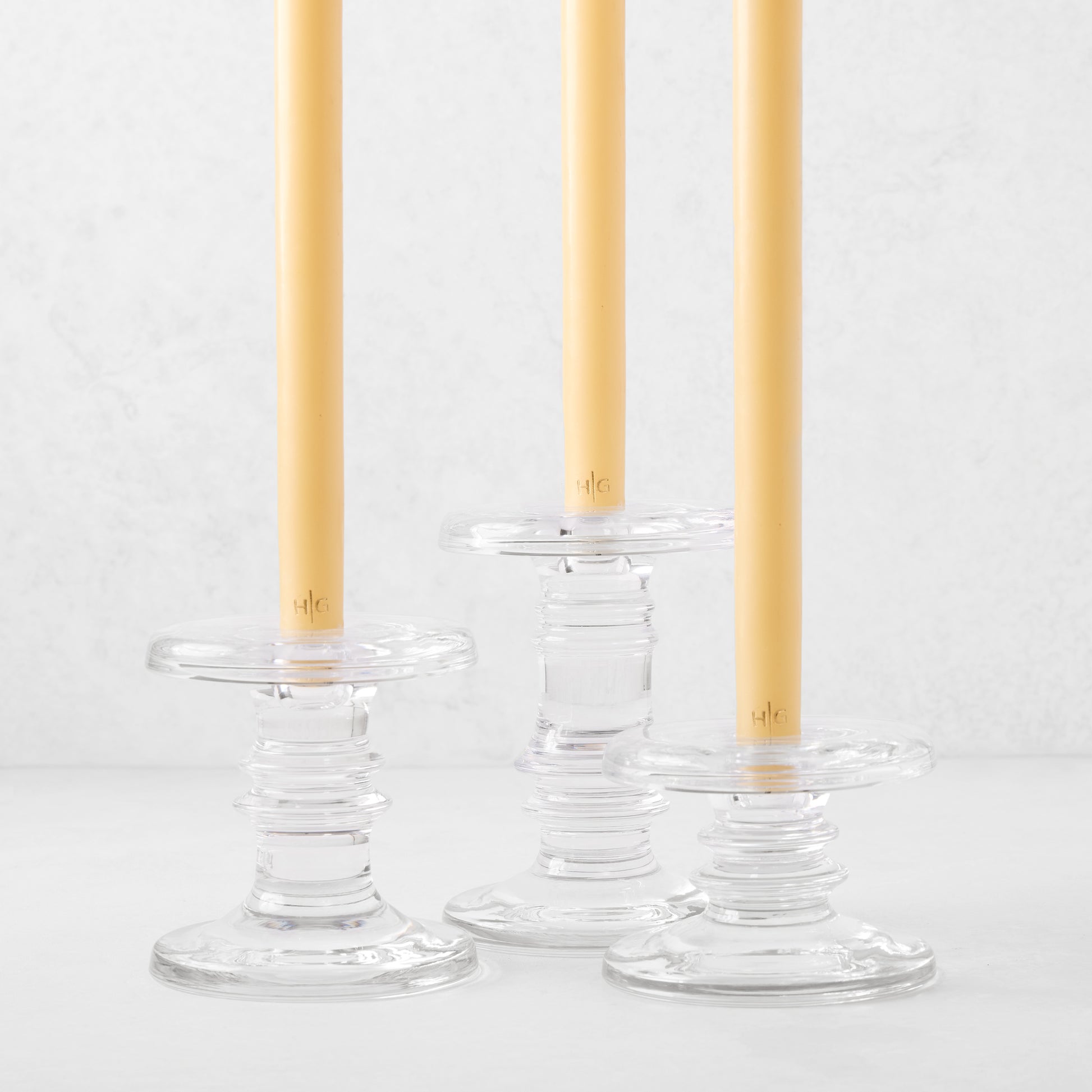 Three clear glass taper candleholders of varying heights with ridged bases, holding yellow taper candles.