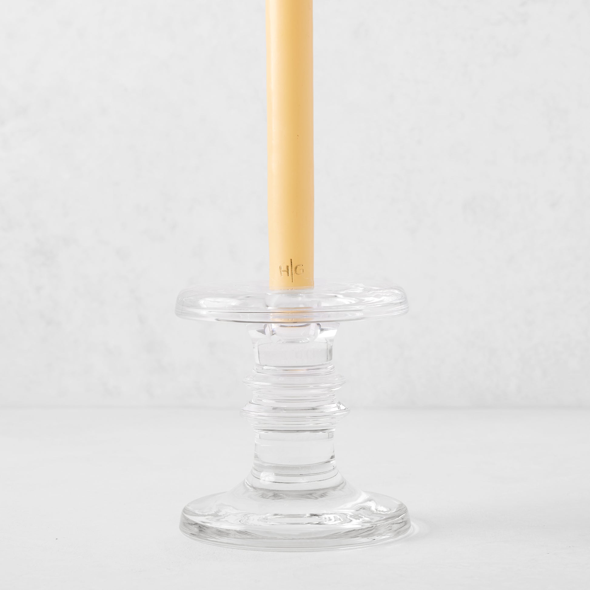 Medium clear glass taper candleholder with ridges, holding a beige taper candle.