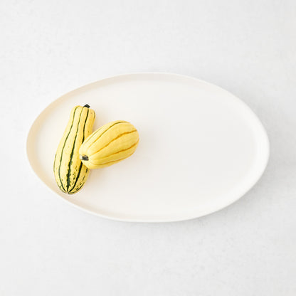 Medium oval white stoneware serving platter with two striped delicata squash on a light surface.