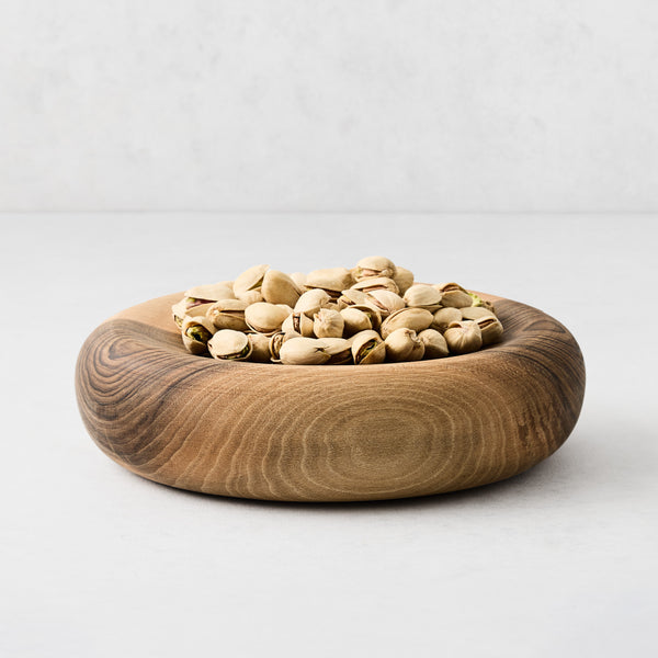 Hand-carved medium walnut wood bowl filled with pistachios, featuring a thick, rounded design and natural wood grain.