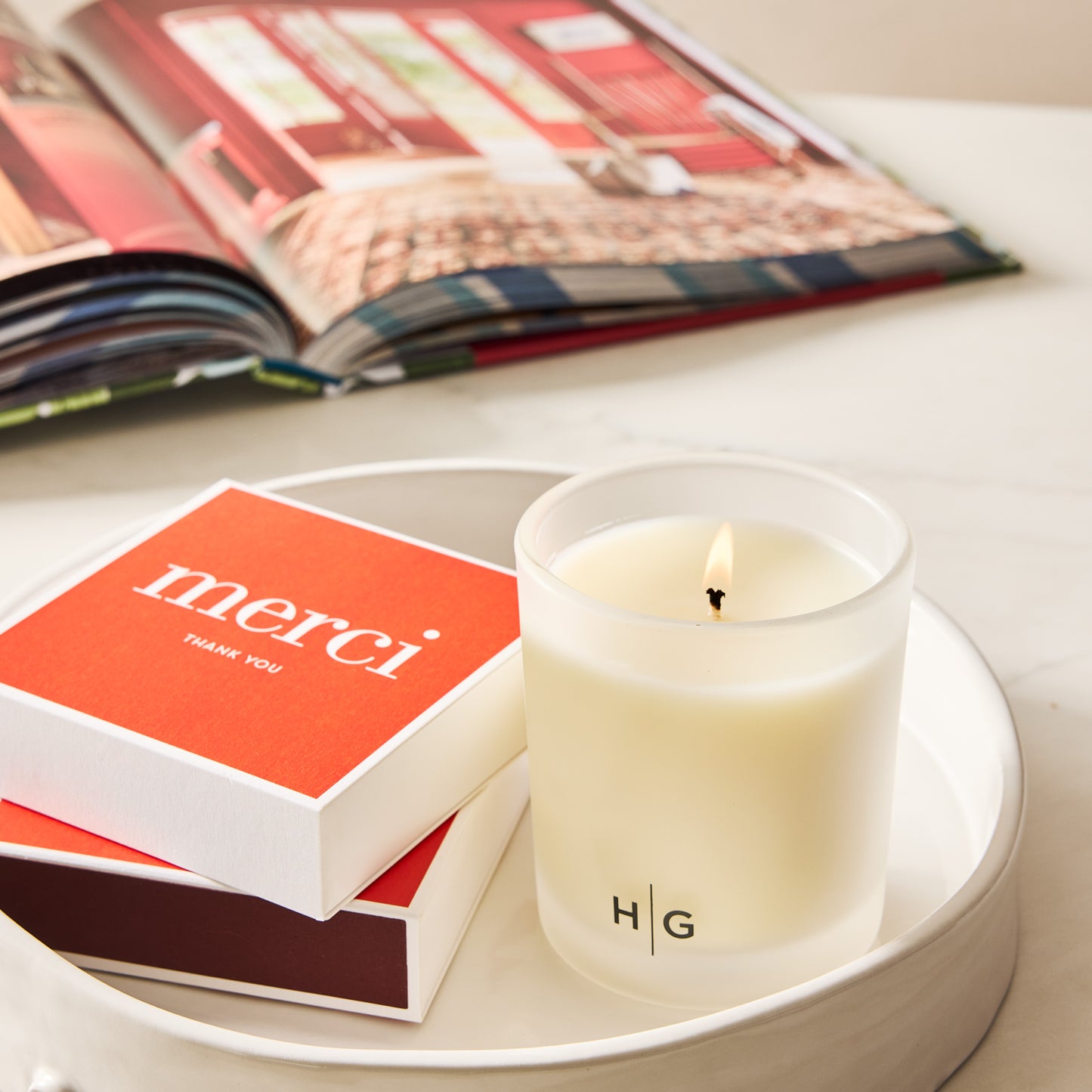 Red "merci" boxed matches with white lettering next to a lit Hudson Grace candle on a white tray.